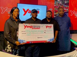 A cheerful winner receives a 1 million naira prize at Yanga FM’s live giveaway event, surrounded by station staff and vibrant branding.